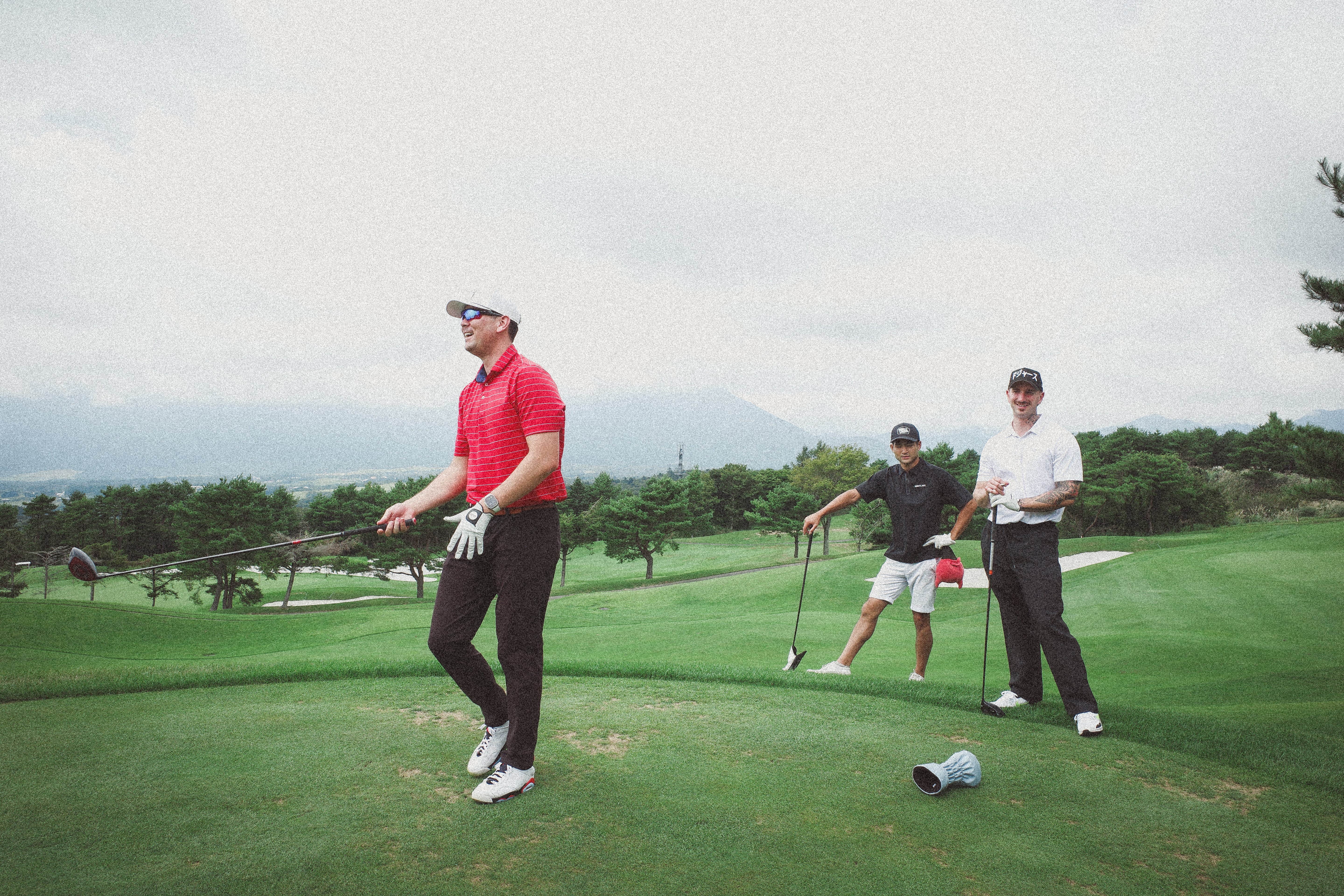 Three golfers on a green course with mountains in the background